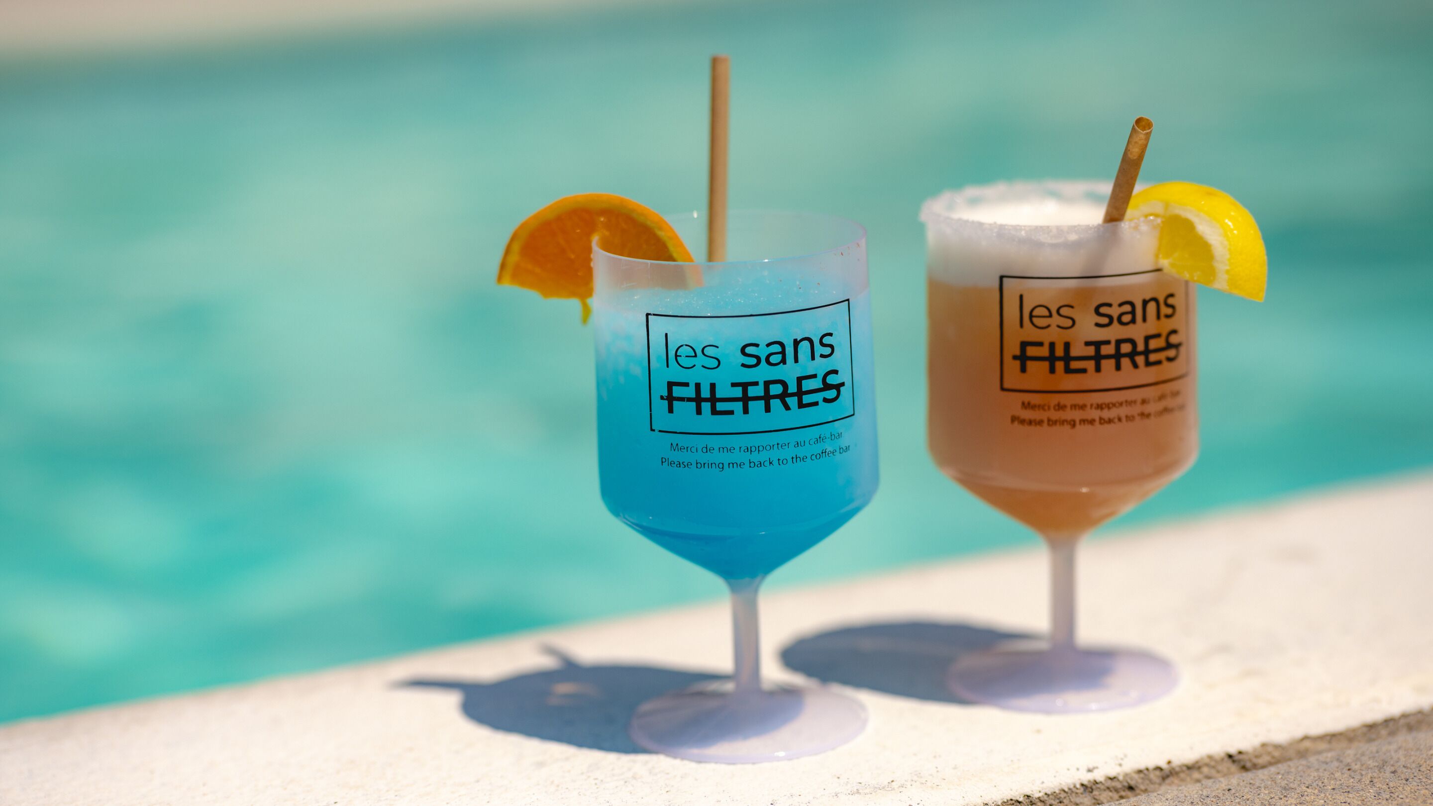 Dos bebidas con etiquetas 'les sans filtres' junto a una piscina.