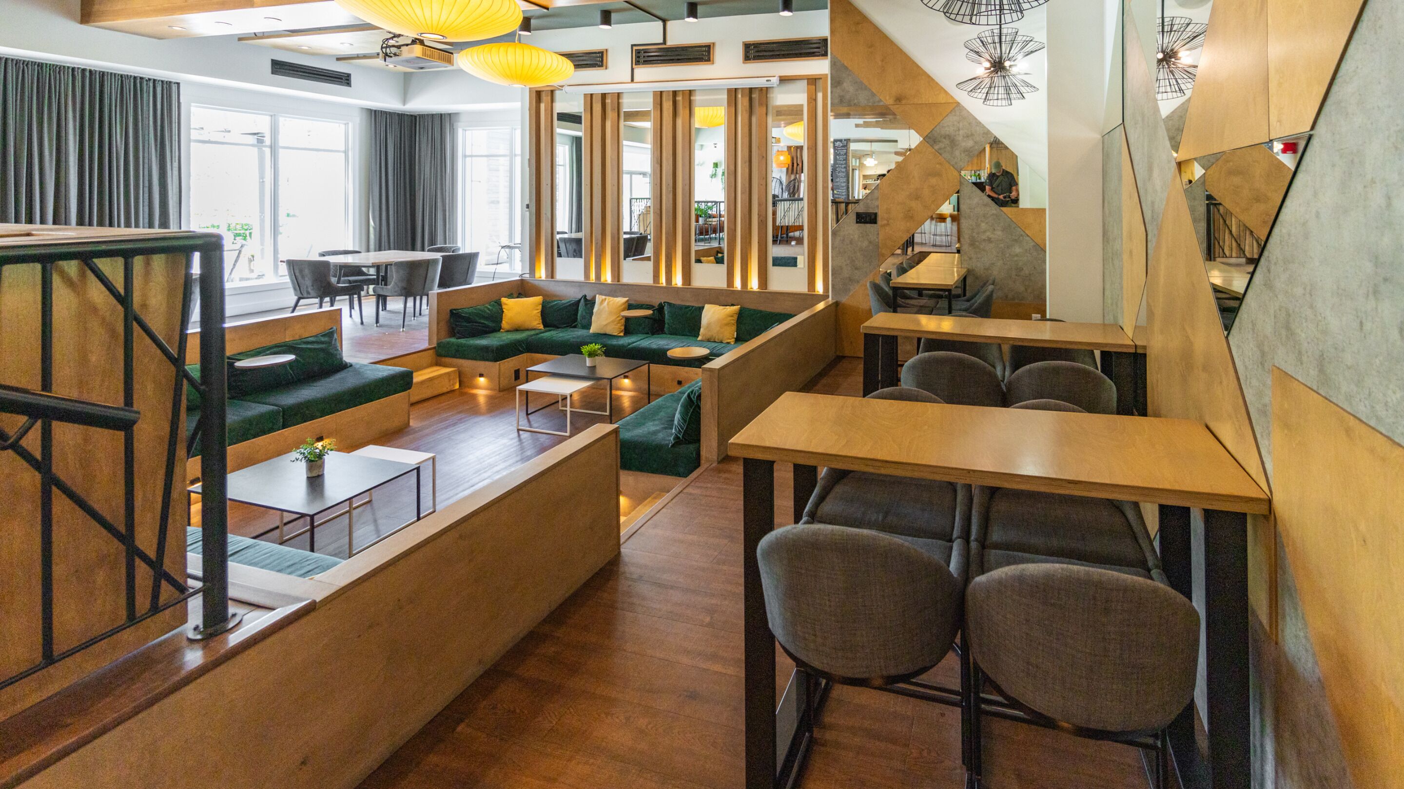 A modern interior with a wooden staircase, green seating areas, and a bar/lounge area.