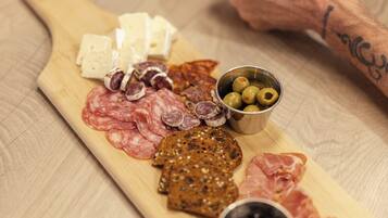 Una tabla de madera con diversos alimentos, entre ellos queso, embutidos, aceitunas y pan.
