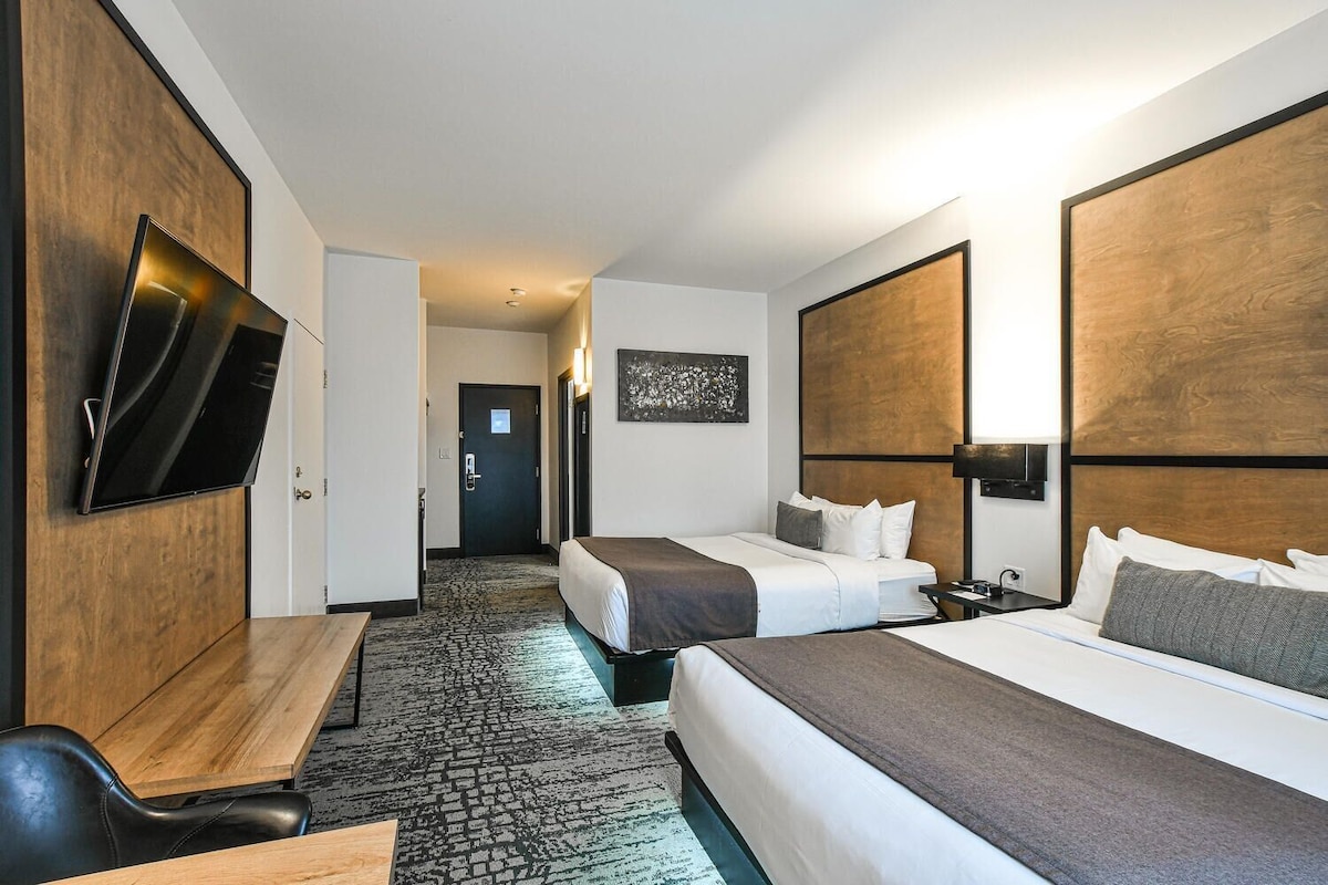 A hotel room with a flat-screen TV, two beds, a desk, and a carpeted floor.