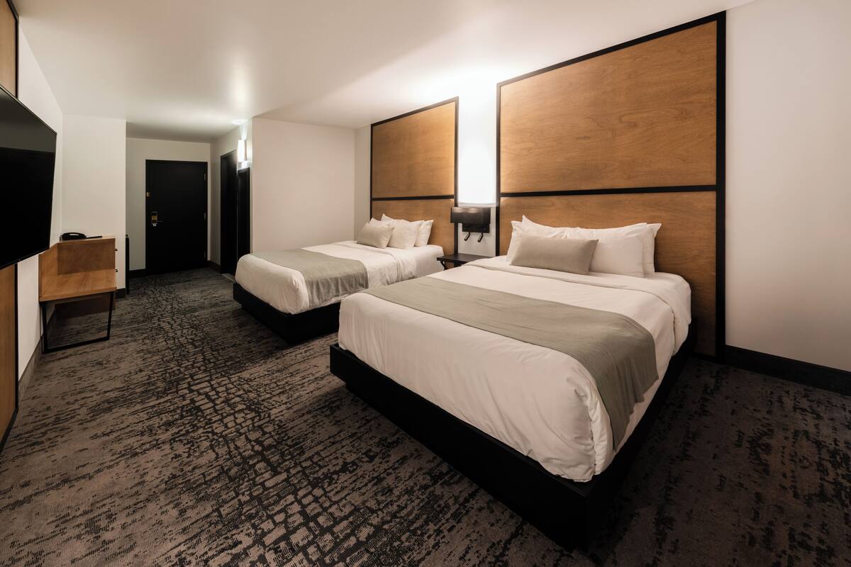Habitación de hotel con dos camas, un televisor de pantalla plana, un escritorio y piso alfombrado.