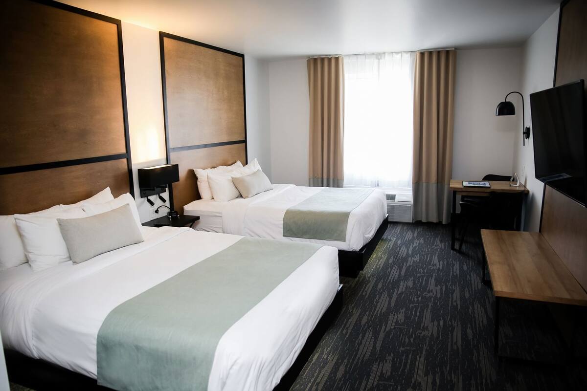 Habitación de hotel con dos camas, un escritorio, un televisor y una ventana con cortinas.