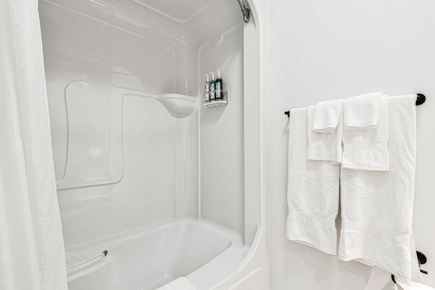 Une salle de bain blanche avec une baignoire, une douche et un porte-serviettes sur lequel sont posées deux serviettes.