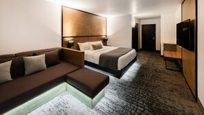 A modern hotel room with a bed, a sofa, a bedside table, a TV, and a carpeted floor.