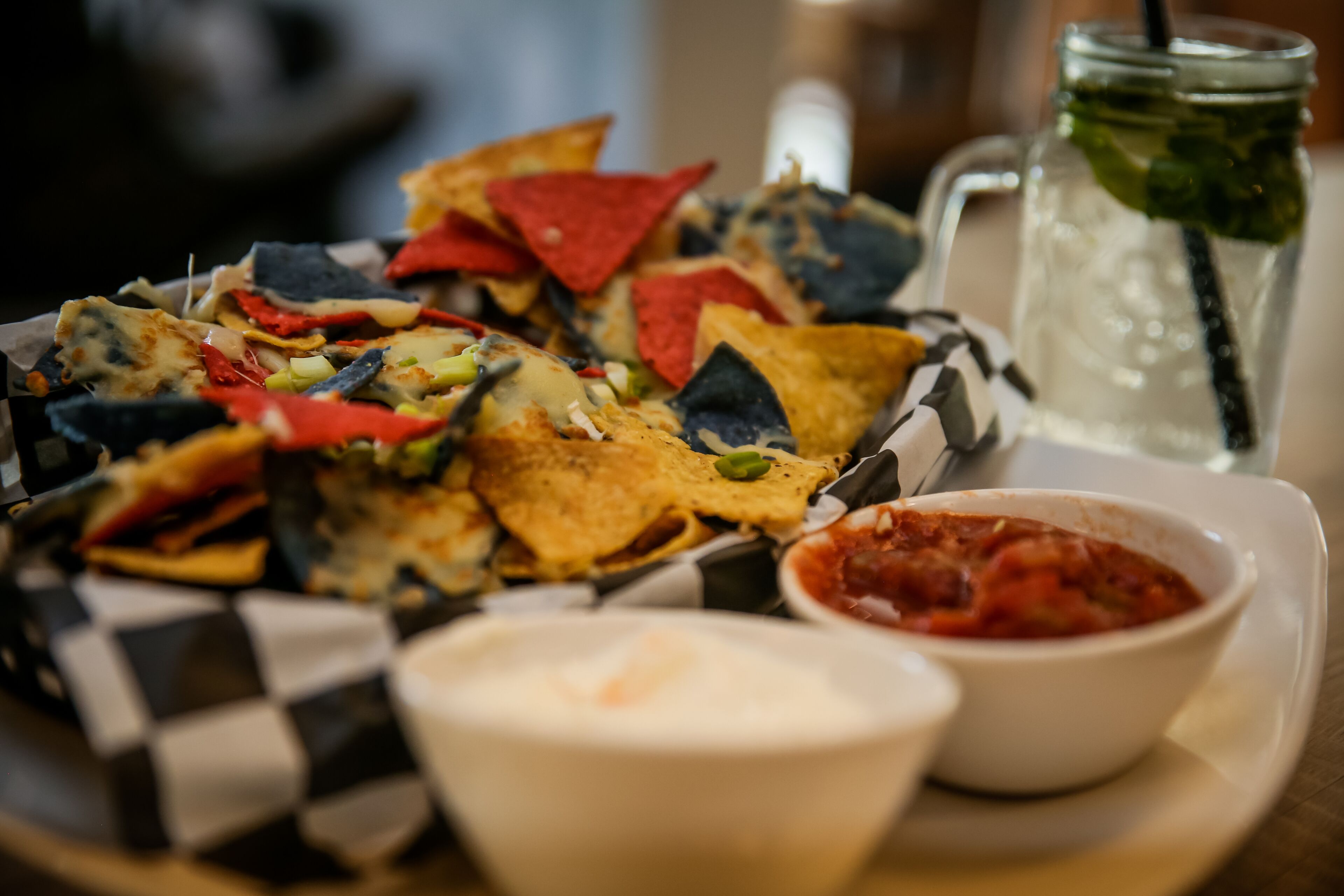 A tray of nachos with various toppings and two small bowls of dipping sauces.