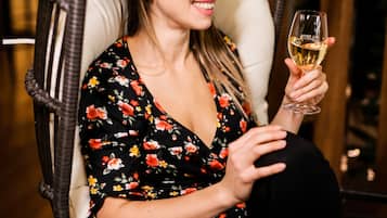 Una persona sentada en una silla de mimbre con cojín, sosteniendo una copa de vino.
