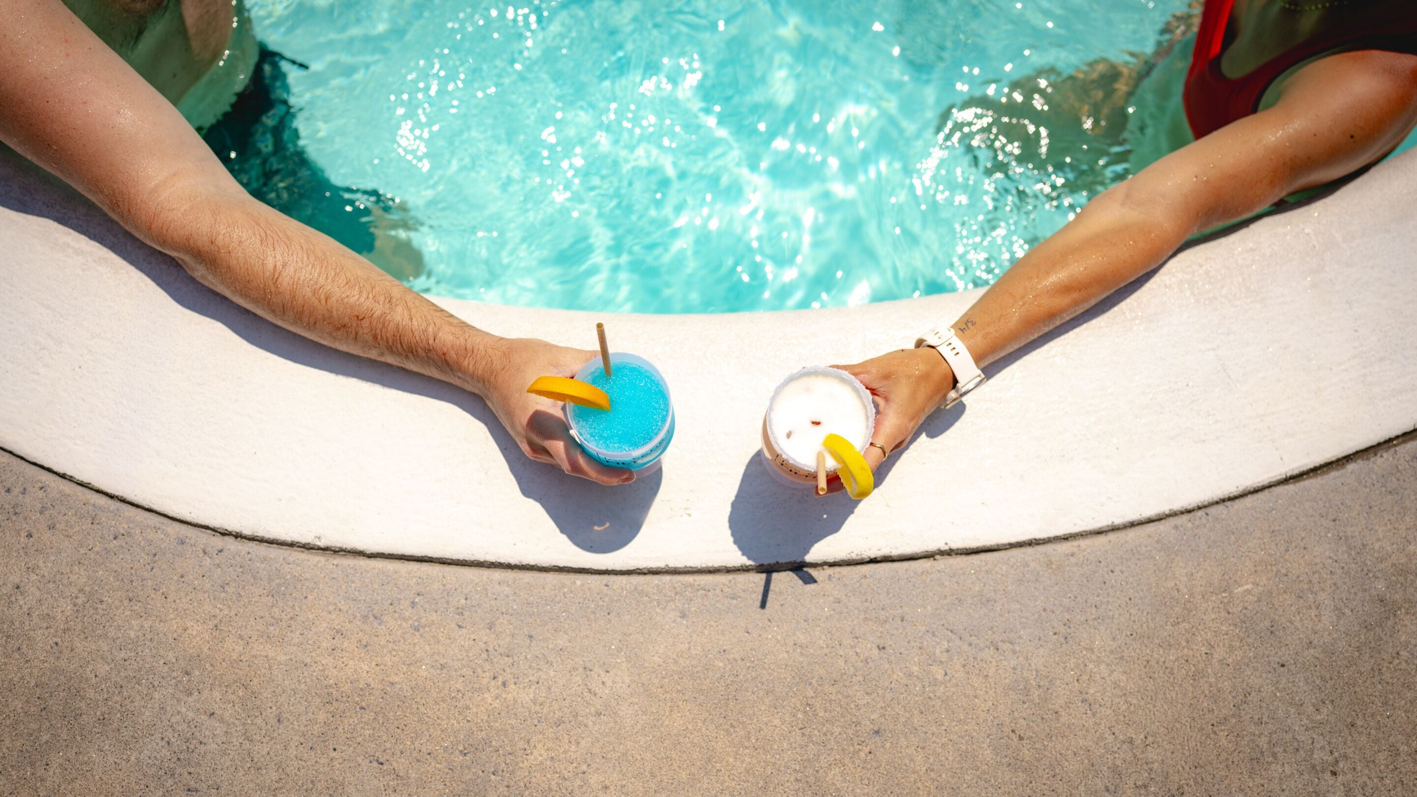 Deux personnes se détendent au bord d’une piscine, un verre à la main.