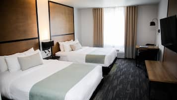 Habitación de hotel con dos camas, un escritorio, un televisor y un amplio ventanal con cortinas.