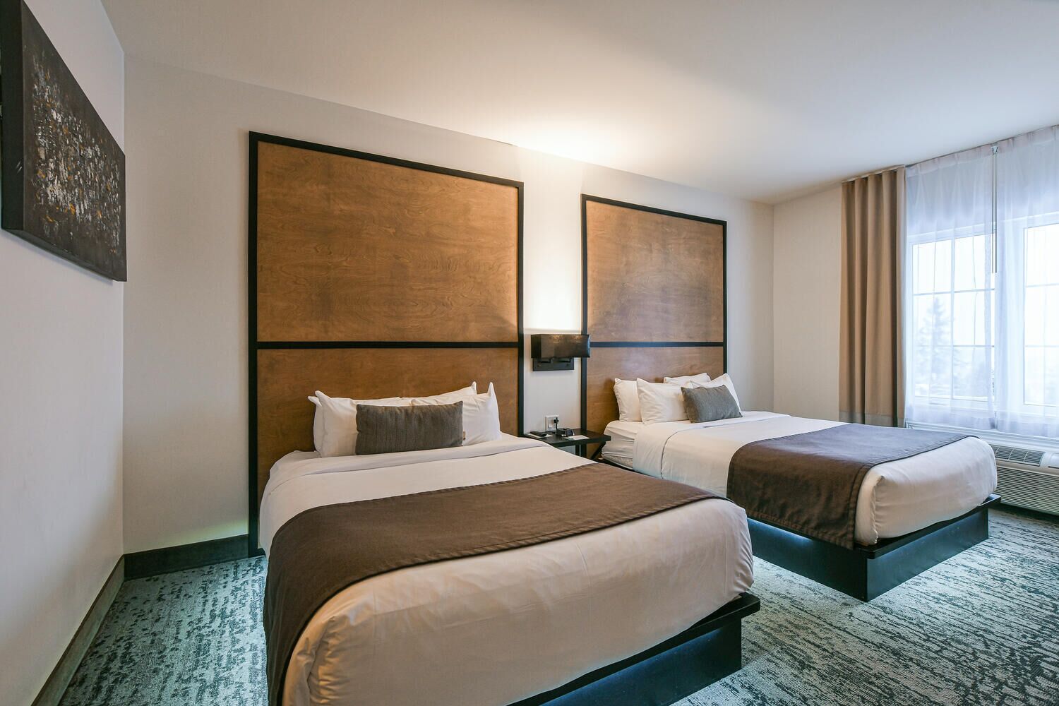 A hotel room with two beds, a large window with curtains, and a wall-mounted light fixture.