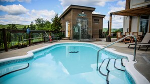A swimming pool with a wooden deck, lounge chairs, and a building with a sign reading "Chute de Vigne frigo".