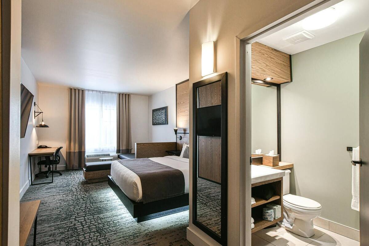 Una habitación de hotel moderna con cama, escritorio, silla y baño con inodoro y lavamanos.