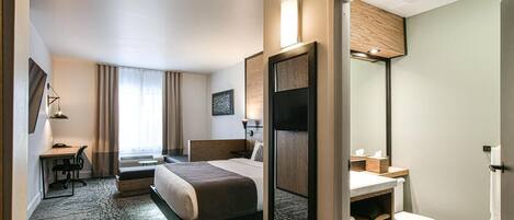A modern hotel room with a bed, desk, chair, and a bathroom with a toilet and sink.