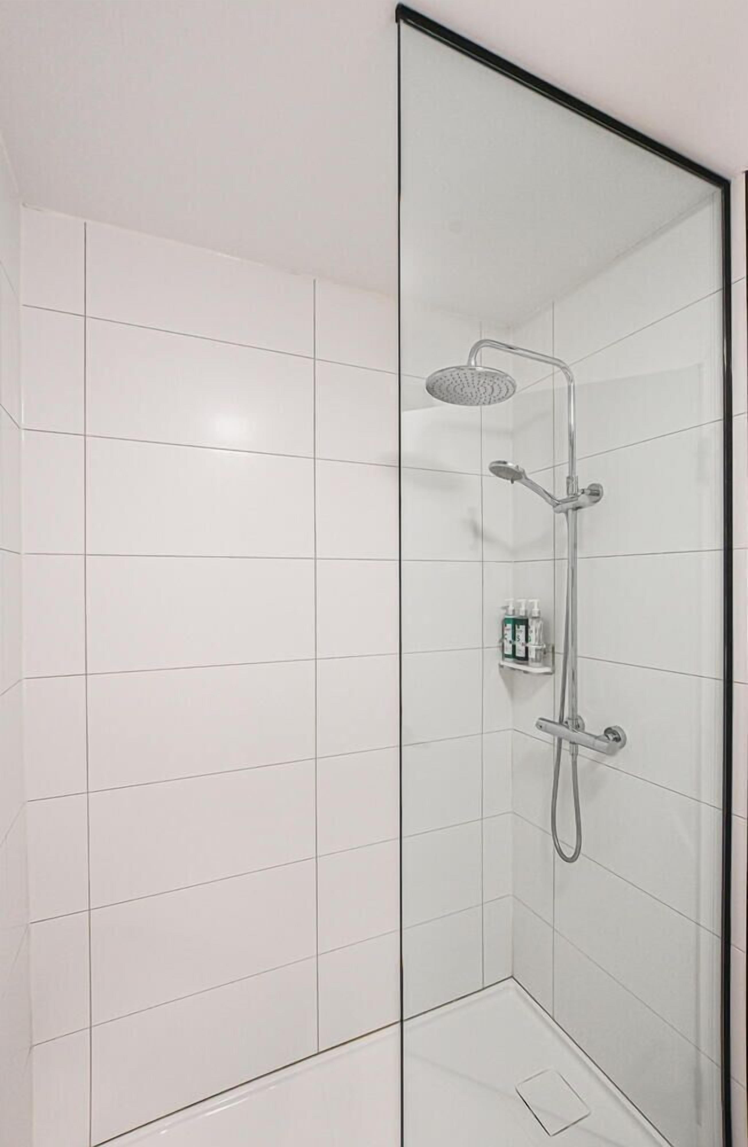 A modern shower with a handheld showerhead and a wall-mounted faucet, set in a corner with white tiled walls.