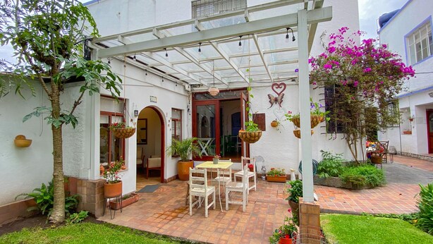 Un patio couvert avec une table et des chaises, entouré de plantes en pot et de suspensions florales.