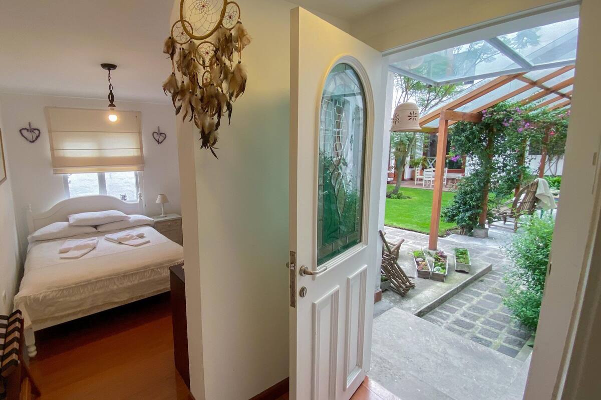 A bedroom with a bed, bedside table, lamp, and a dreamcatcher hanging from the ceiling.