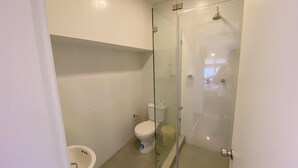 Une salle de bain équipée de toilettes, d’un bidet et d’une douche à parois de verre.