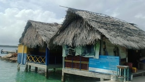 Zwei mit Strohdach versehene Gebäude mit blauer und gelber Fassade, die über dem Wasser stehen, mit einem sichtbaren Schild.