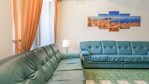A room with a green sofa, a patterned rug, and a wall with a cityscape painting. - Hotel La Pergoletta (Massa Lubrense)