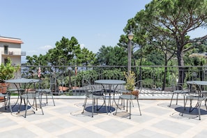 An outdoor patio with round tables and metal chairs, surrounded by a metal fence and trees. - Hotel La Pergoletta (Massa Lubrense)