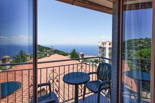 A balcony with a table and chairs, offering a view of the sea and surrounding buildings. - Hotel La Pergoletta (Massa Lubrense)