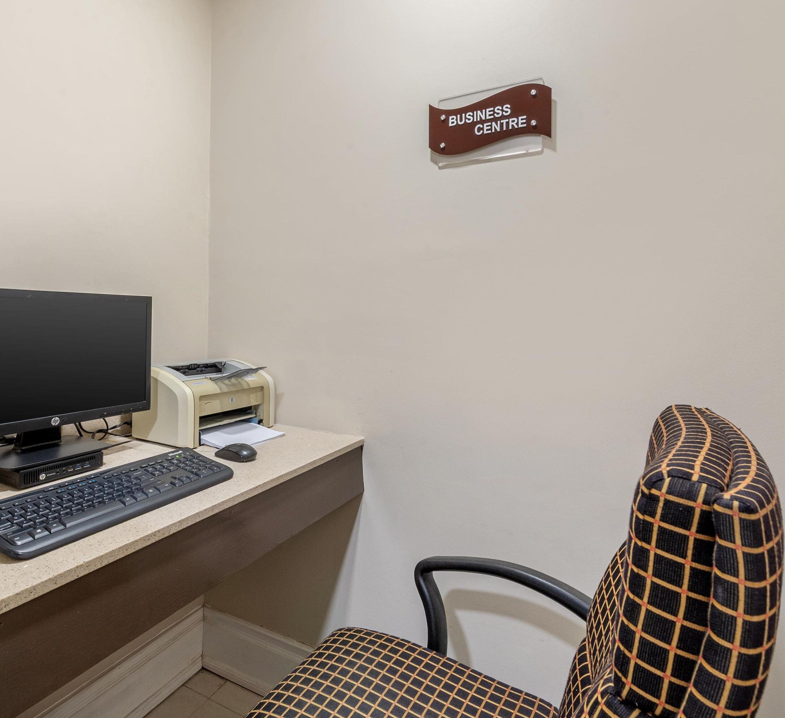Un centro de negocios con un ordenador de escritorio, una impresora, teclado, ratón y una silla de oficina con estampado.