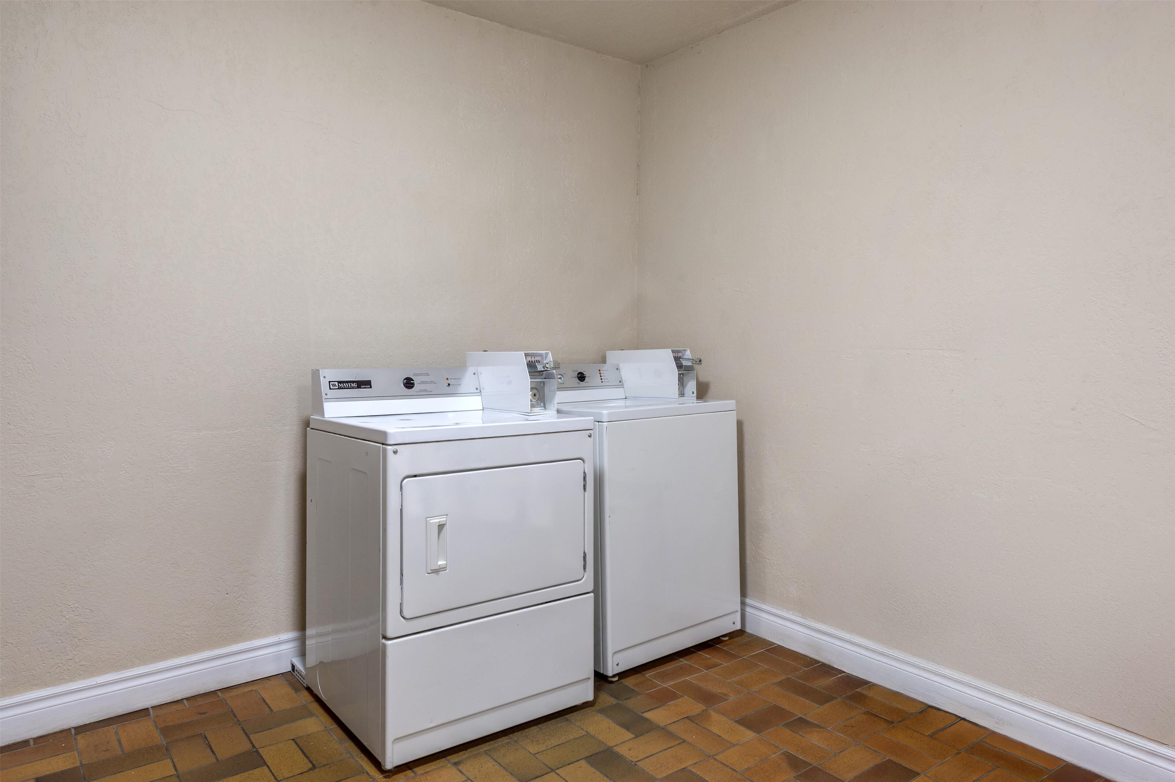 A laundry room with two stacked washers and dryers, white walls, and a wooden floor.
