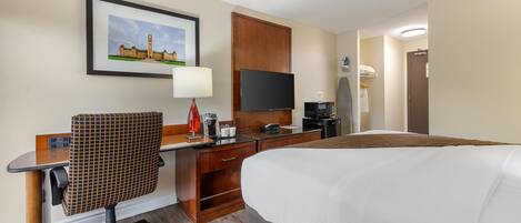 A hotel room with a bed, a desk with a chair, a television, a coffee maker, and a framed picture on the wall.