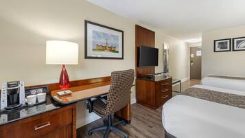 A hotel room with a desk, chair, bed, TV, and a framed picture of a building.