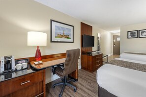 A hotel room with a desk, chair, bed, TV, and a framed picture of a building.