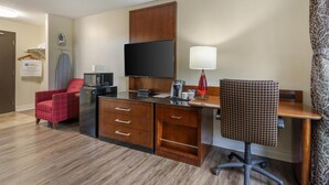 A hotel room with a wooden desk, a red armchair, a TV, a lamp, and a coffee maker. - SureStay Hotel by Best Western Kemptville (North Grenville)