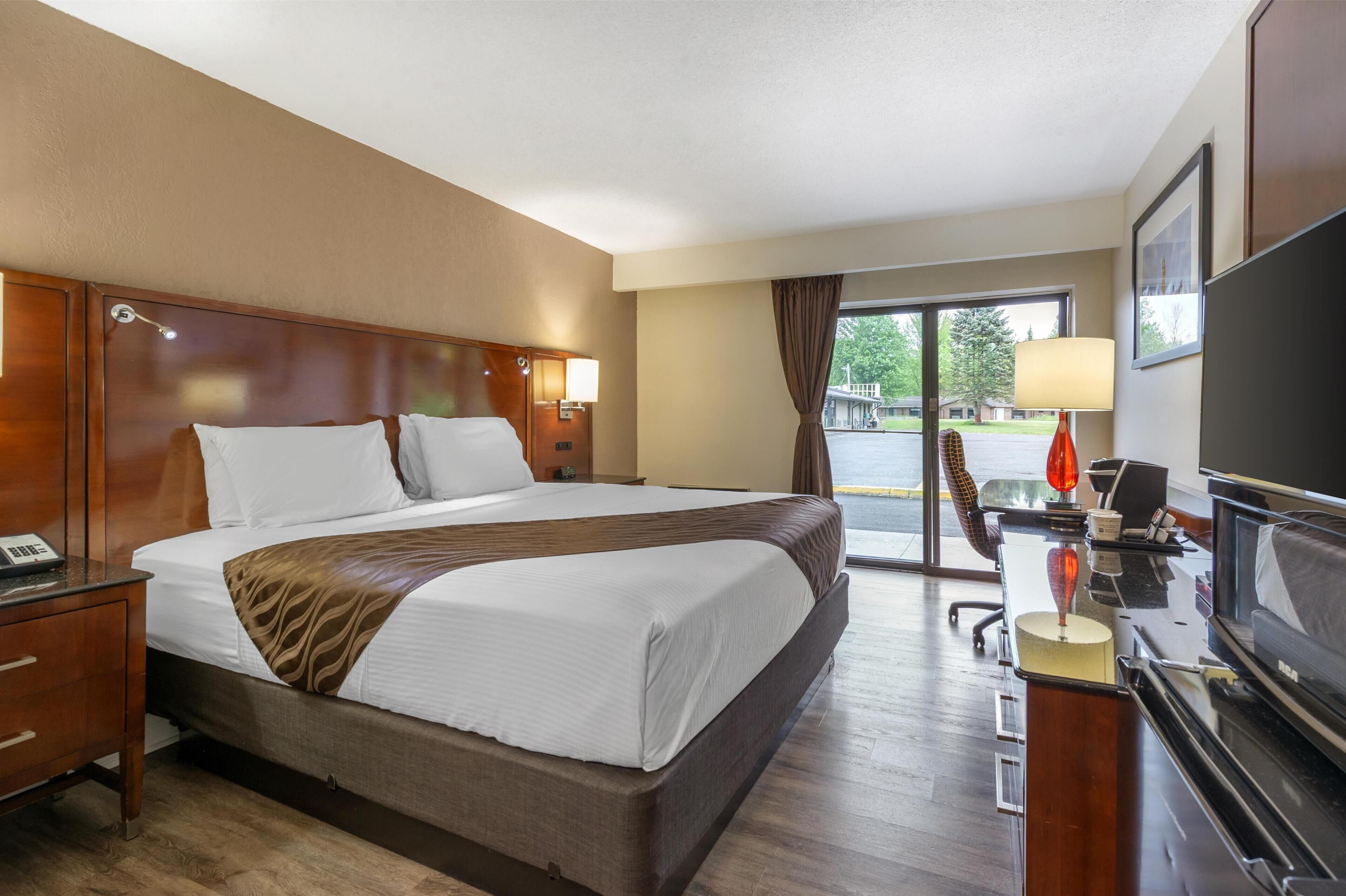 Habitación de hotel con una cama grande, un escritorio con computadora, un televisor y una ventana con cortinas.