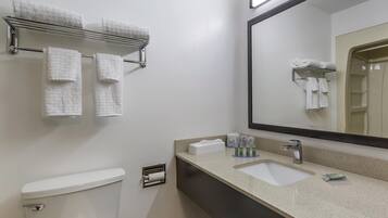 A bathroom with a toilet, sink, and a mirror. There are towels on a rack and a shelf, and toiletries on the sink counter.