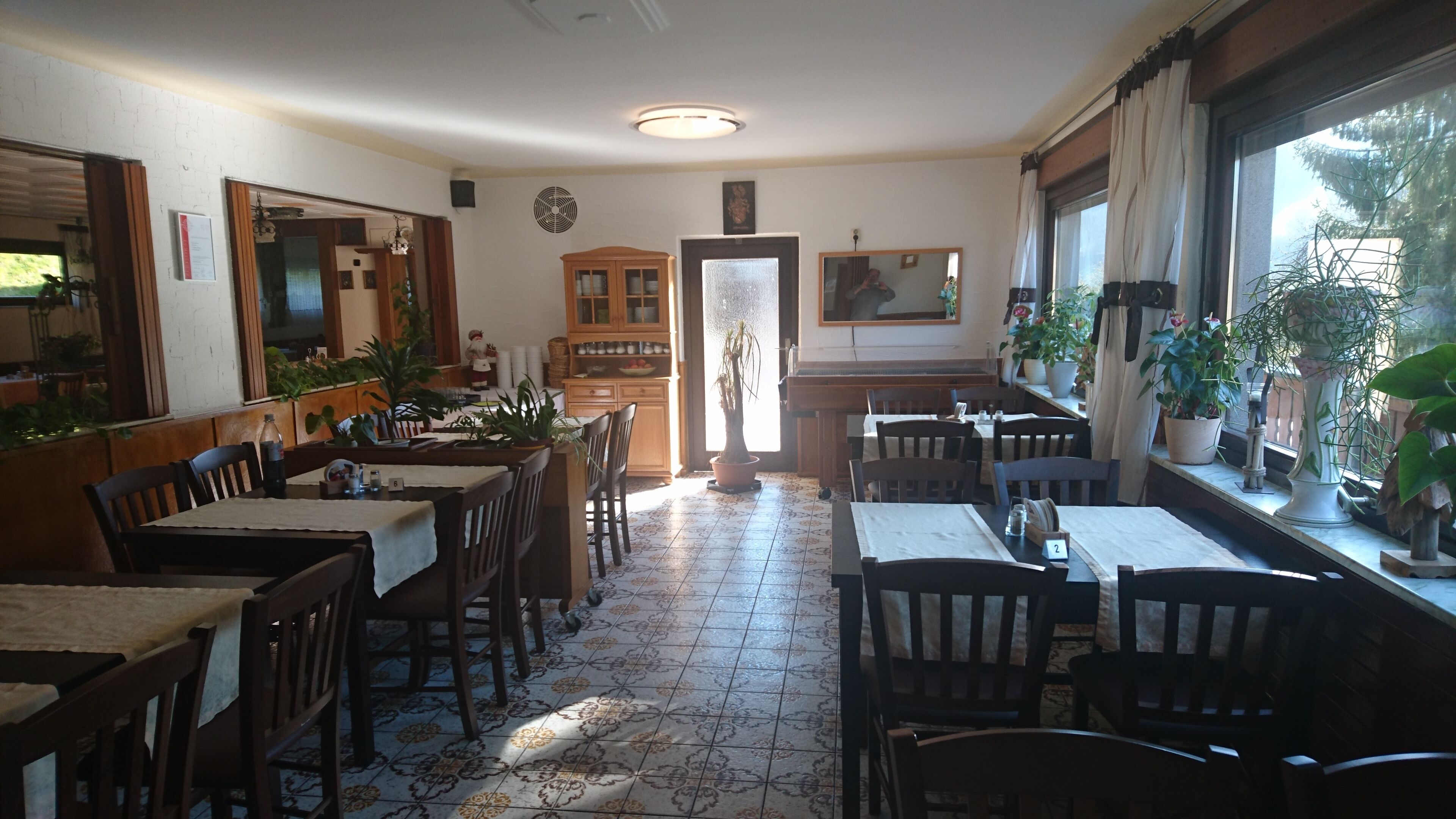 A restaurant with wooden tables and chairs, a tiled floor, and potted plants.