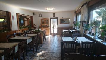 A restaurant with wooden tables and chairs, a tiled floor, and potted plants.