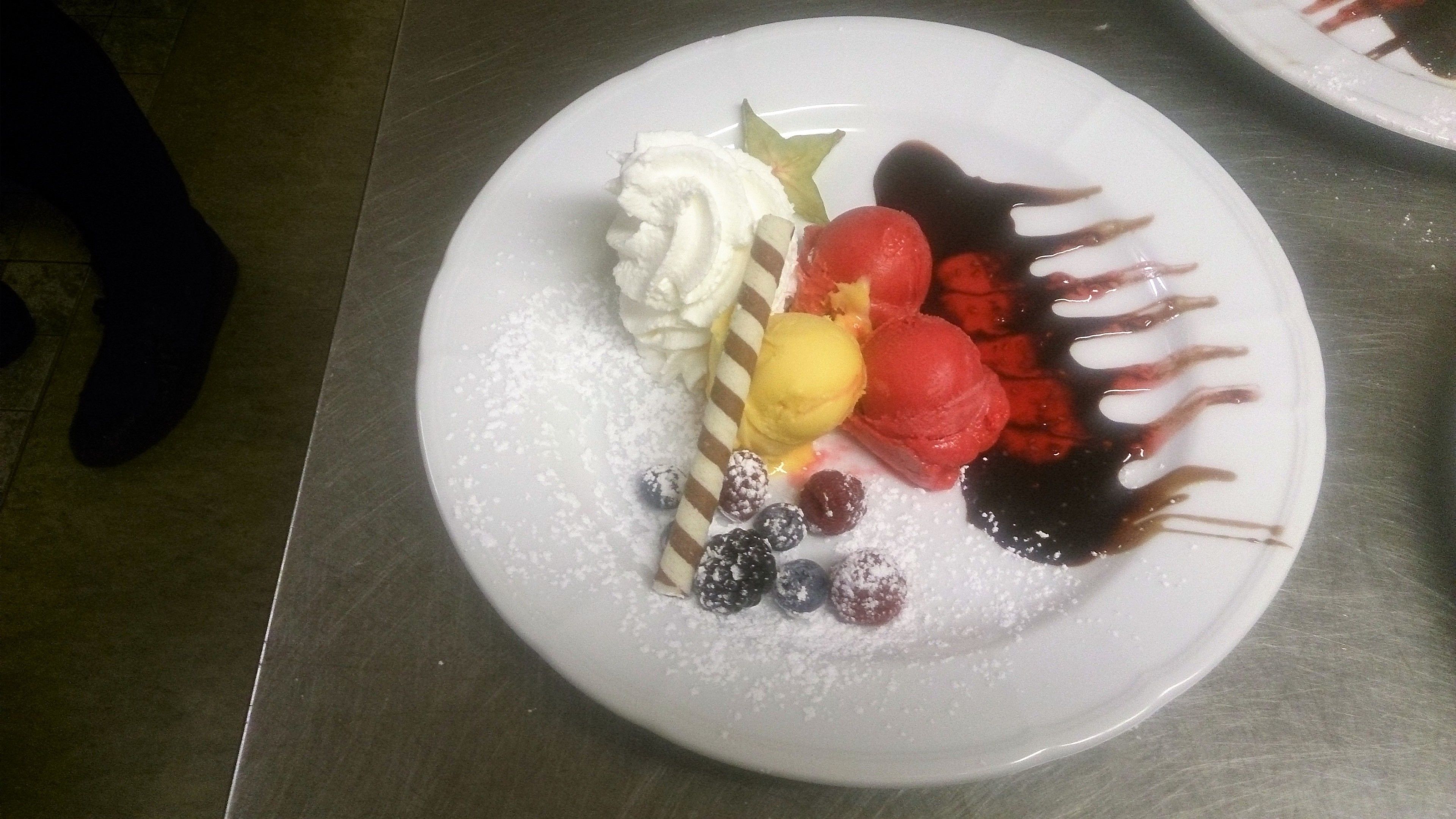 Un plato de postre con crema batida, fruta y salsa de chocolate.
