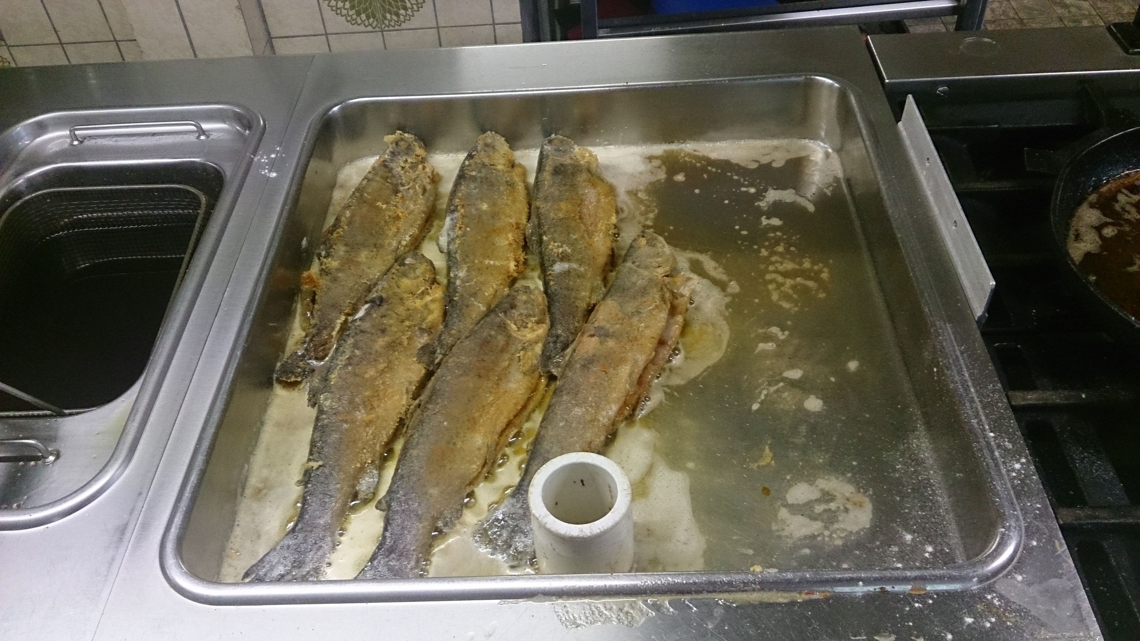 Ein Spülbecken, über dem mehrere Fische gebraten werden.