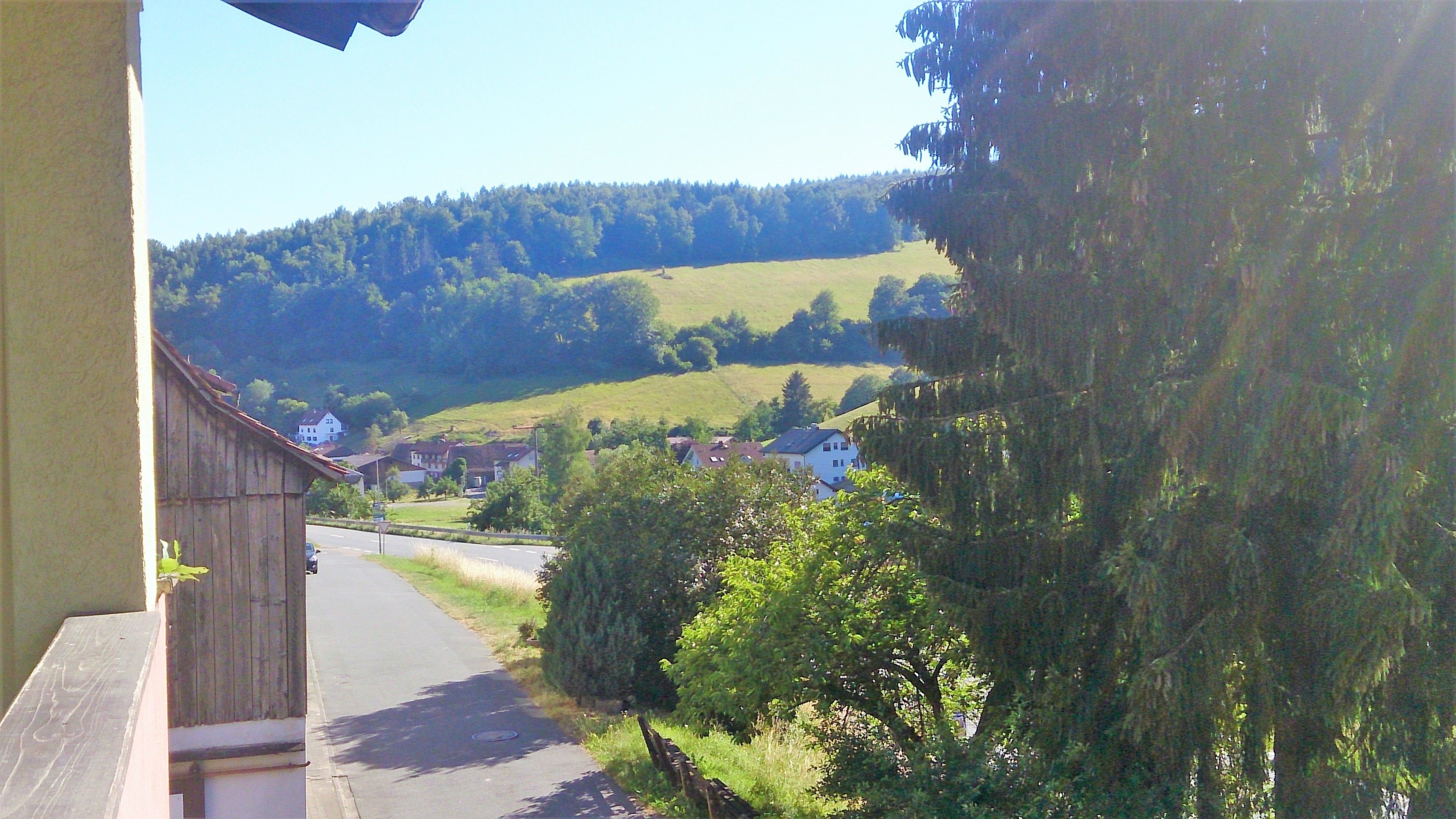 A rural street with houses, a wooden fence, and a hill in the background.
