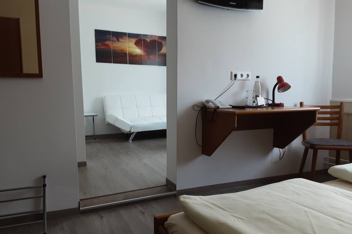 Une chambre d’hôtel avec un lit, un bureau avec une lampe, une chaise, un téléviseur fixé au mur et un tableau au-dessus du bureau.