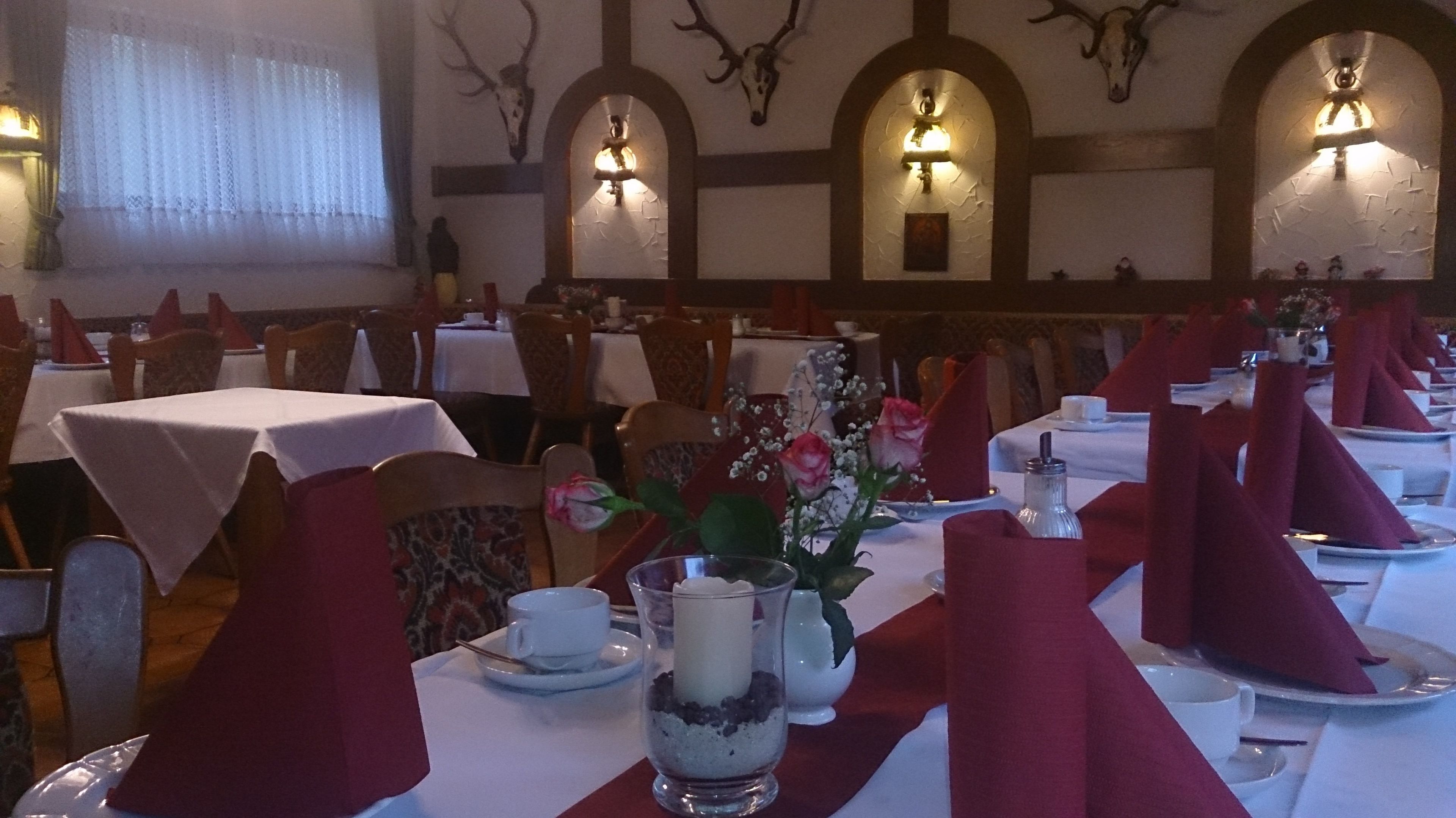 Um restaurante com várias mesas montadas para refeições, cada uma com uma toalha vermelha e um arranjo de velas.