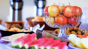 A table with a glass bowl containing apples, a plate with watermelon slices, and a coffee maker in the background. - Pratico Hotel (Santarém)