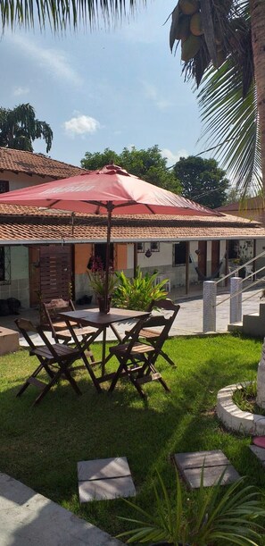 An outdoor patio with a red umbrella, wooden chairs, and a small table. - Pousada Mato Grosso (Santarém)