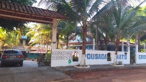 Uma entrada gradeada com palmeiras, um carro e um edifício com a placa "QUEADA MATU GROSSO".
