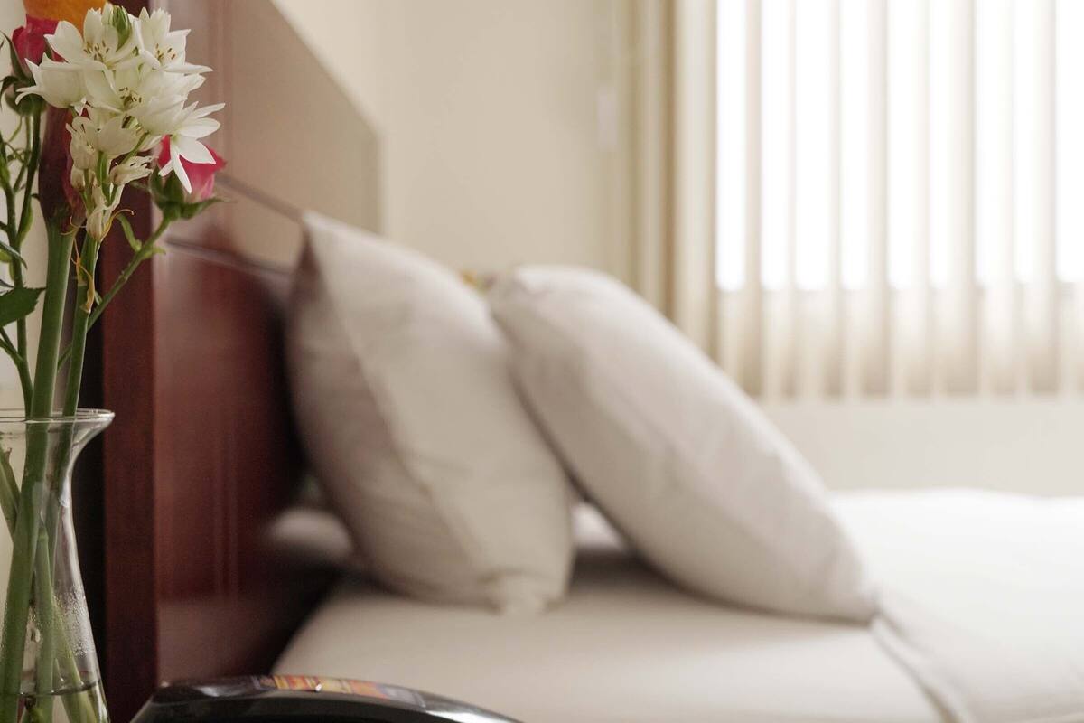 A bed with white pillows and a vase with flowers on a bedside table.