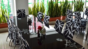 Ein moderner Essbereich mit einem schwarzen Tisch und Stühlen, einer Vase mit einer roten Rose und Zimmerpflanzen im Hintergrund.
