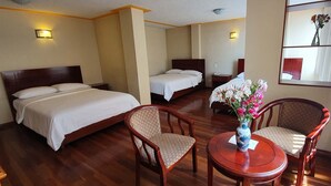 Ein Hotelzimmer mit zwei Betten, einer Sitzecke mit Tisch und Stühlen sowie einem Blumenstrauß.