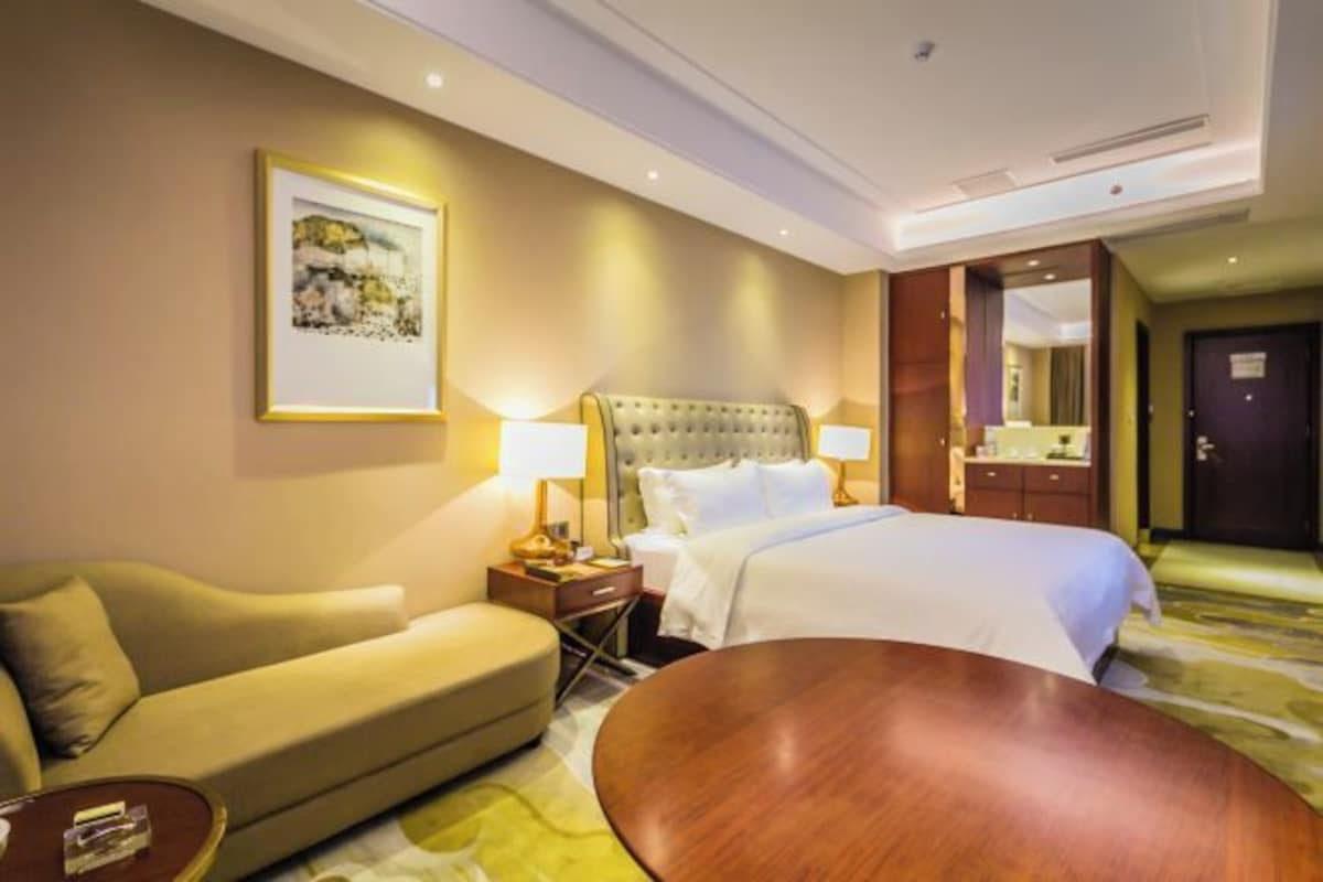 Une chambre d’hôtel avec un grand lit, un canapé, une table basse en bois et un tableau au mur.