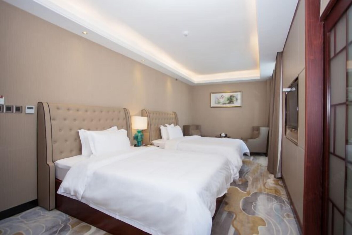 A hotel room with two beds, a large window, and a carpeted floor.