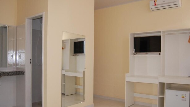Una habitación con cama, espejo, televisor y un armario blanco.