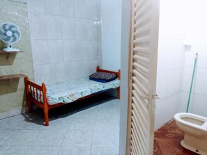 A small, tiled bathroom with a wooden bench, a toilet, and a fan. - Espaço Hostel Barra Funda (São Paulo)