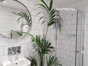 A bathroom with white tiled walls, a glass shower enclosure, a sink with a mirror, and a potted plant.
